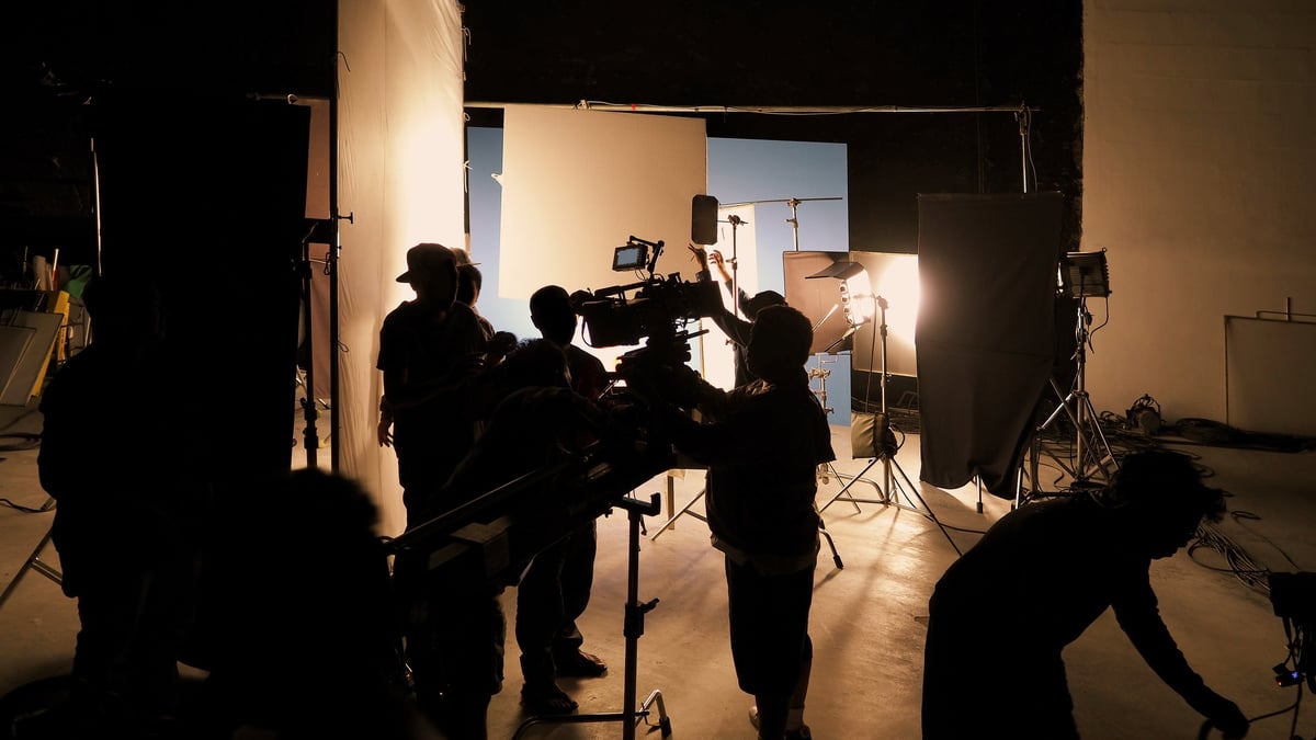 Film crew and camera on a dolly crane amid dramatic studio lighting